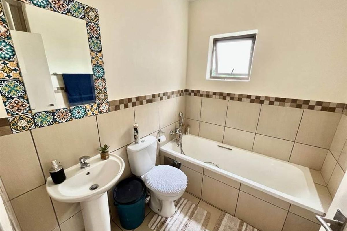 A functional bathroom featuring a pedestal basin, a built-in bathtub, and decorative tiled wall accents, providing a practical space with neutral finishes.