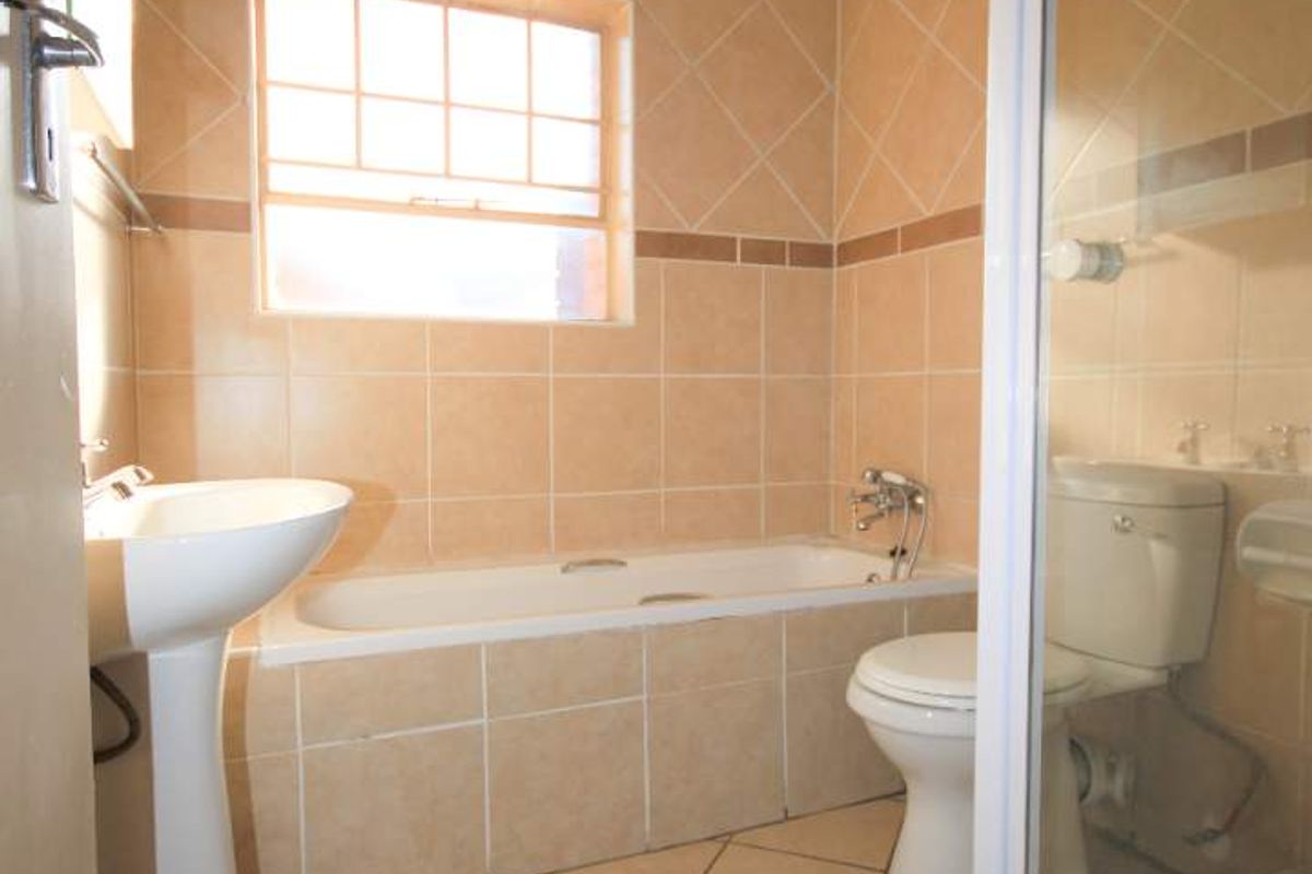 A functional bathroom featuring a pedestal basin, built-in bathtub, and a separate shower enclosure with neutral ceramic tiling throughout.