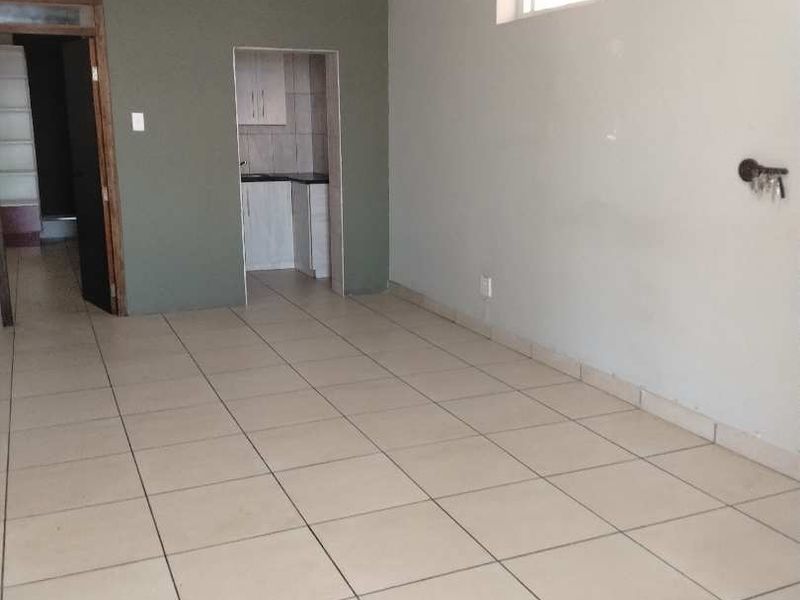 An empty office space featuring tiled flooring, neutral wall finishes, and a small built-in kitchenette area.