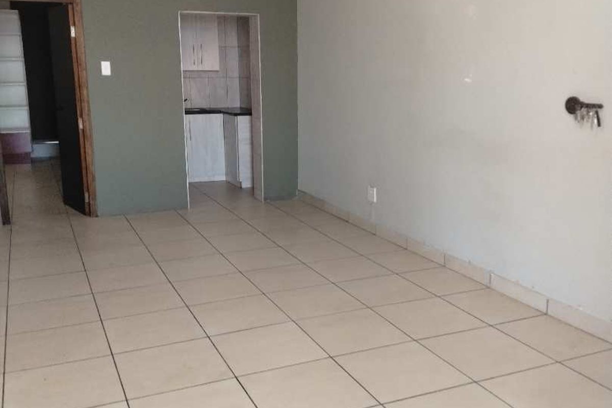 An empty office space featuring tiled flooring, neutral wall finishes, and a small built-in kitchenette area.