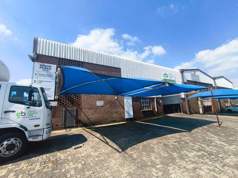 Industrial property exterior featuring a brick facade, corrugated metal roofing, and a paved driveway with installed shade cloth carports.