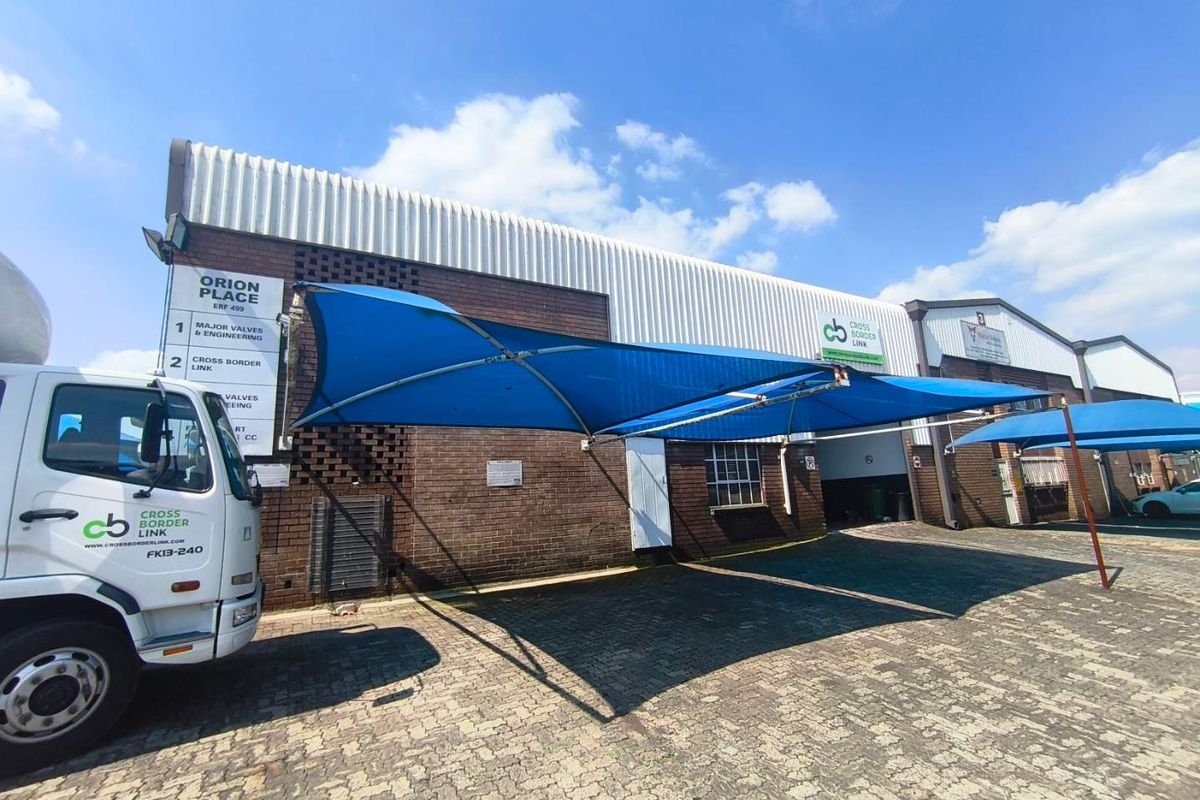 Industrial property exterior featuring a brick facade, corrugated metal roofing, and a paved driveway with installed shade cloth carports.
