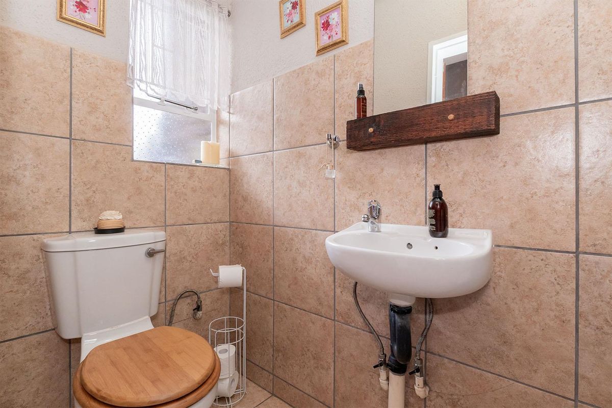 A compact guest bathroom featuring floor-to-ceiling beige wall tiles, a wall-mounted basin, and a standard toilet.