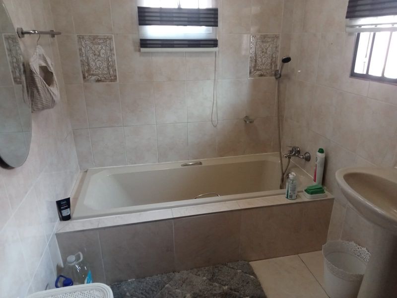 A functional bathroom featuring a built-in bathtub, pedestal basin, and neutral wall tiling, offering a standard layout with potential for modern updates.