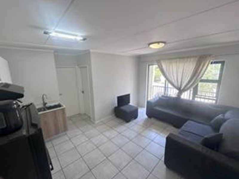 Open-plan living area featuring tiled flooring, a compact kitchenette with sink, and sliding door access to an outdoor space.