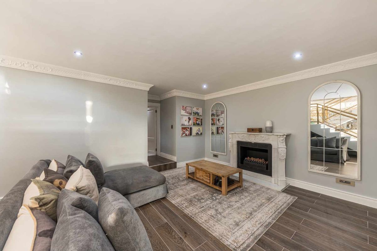 A well-maintained living room featuring a decorative fireplace, crown molding, and modern wood-look tile flooring with recessed ceiling lighting.