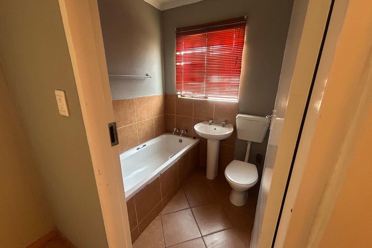 A functional bathroom featuring a bathtub with tiled surround, pedestal basin, and toilet, finished with ceramic floor tiles and a window with blinds.