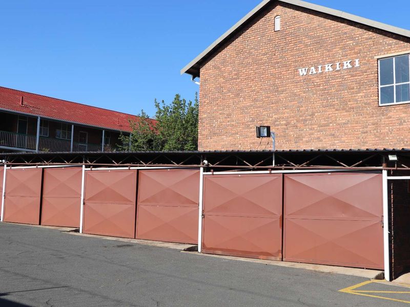 A row of secure metal garage units located at the Waikiki apartment complex, featuring brick exterior walls and a paved driveway.