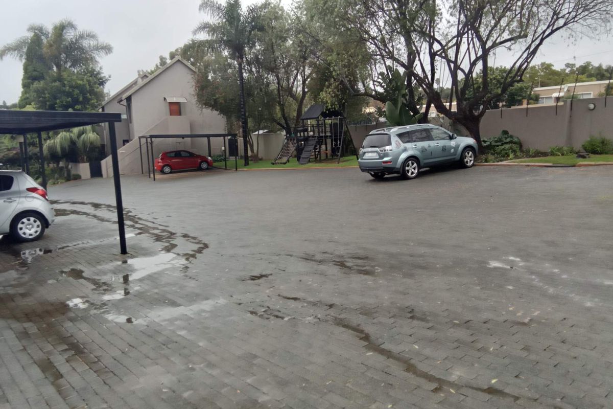A paved communal parking area with covered carports and surrounding landscaped garden space within the apartment complex.