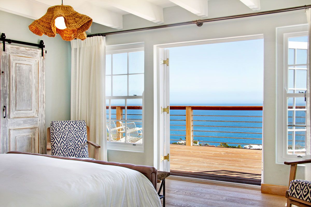 Bright bedroom featuring exposed ceiling beams, hardwood floors, and direct access to a private balcony with expansive ocean views.
