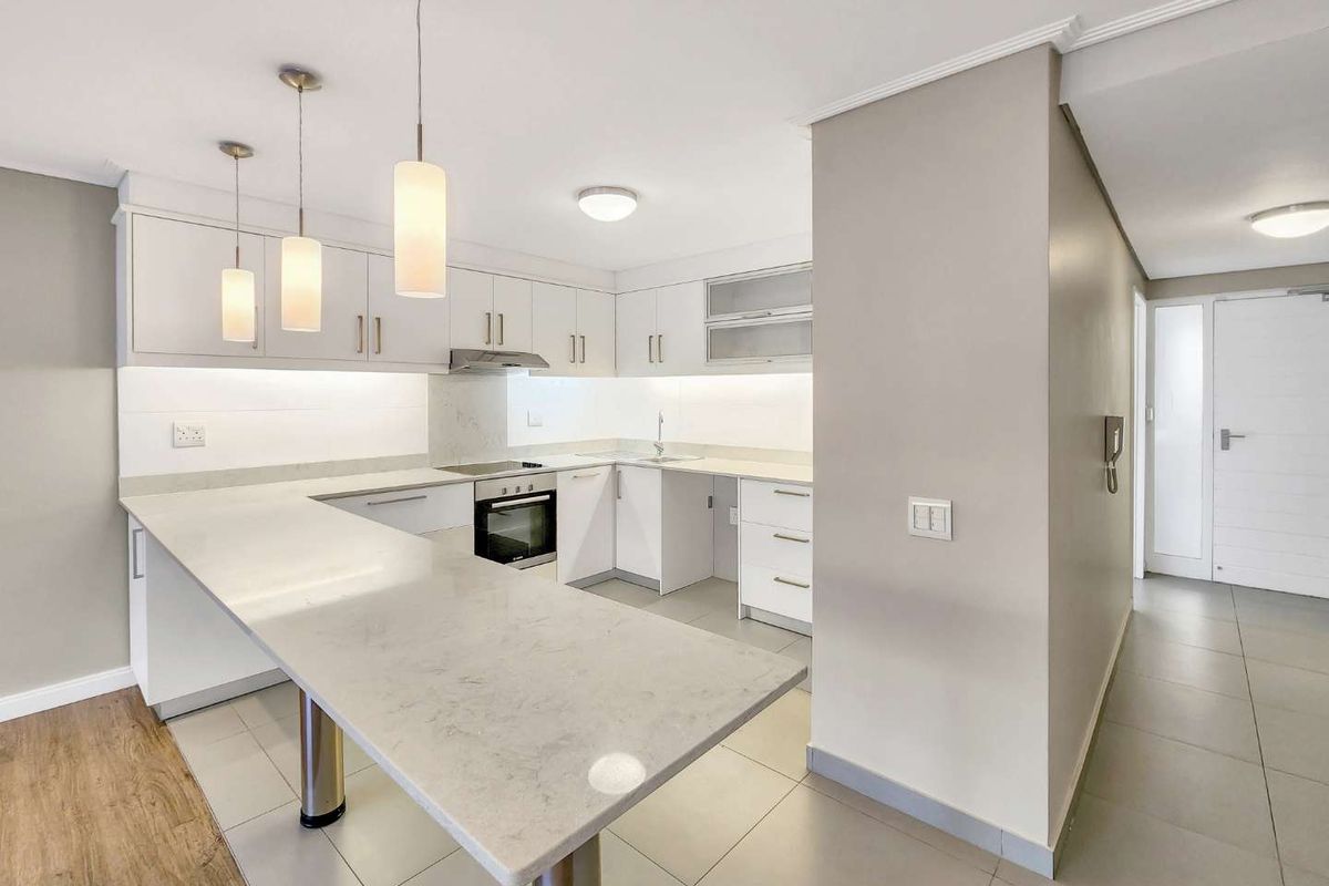 Modern kitchen featuring white cabinetry, quartz countertops, integrated oven and hob, and a breakfast bar, finished with sleek tiled flooring and contemporary lighting.