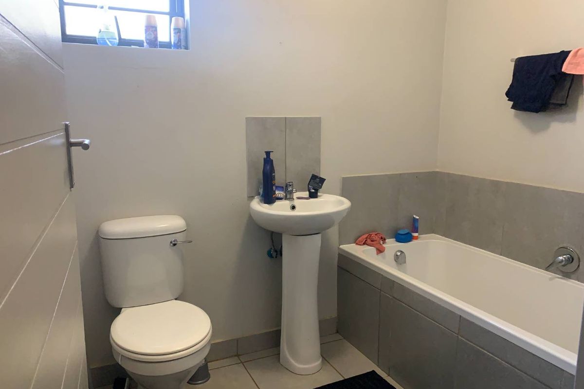 A functional bathroom featuring a pedestal basin, a standard toilet, and a tiled bathtub with a neutral color palette.