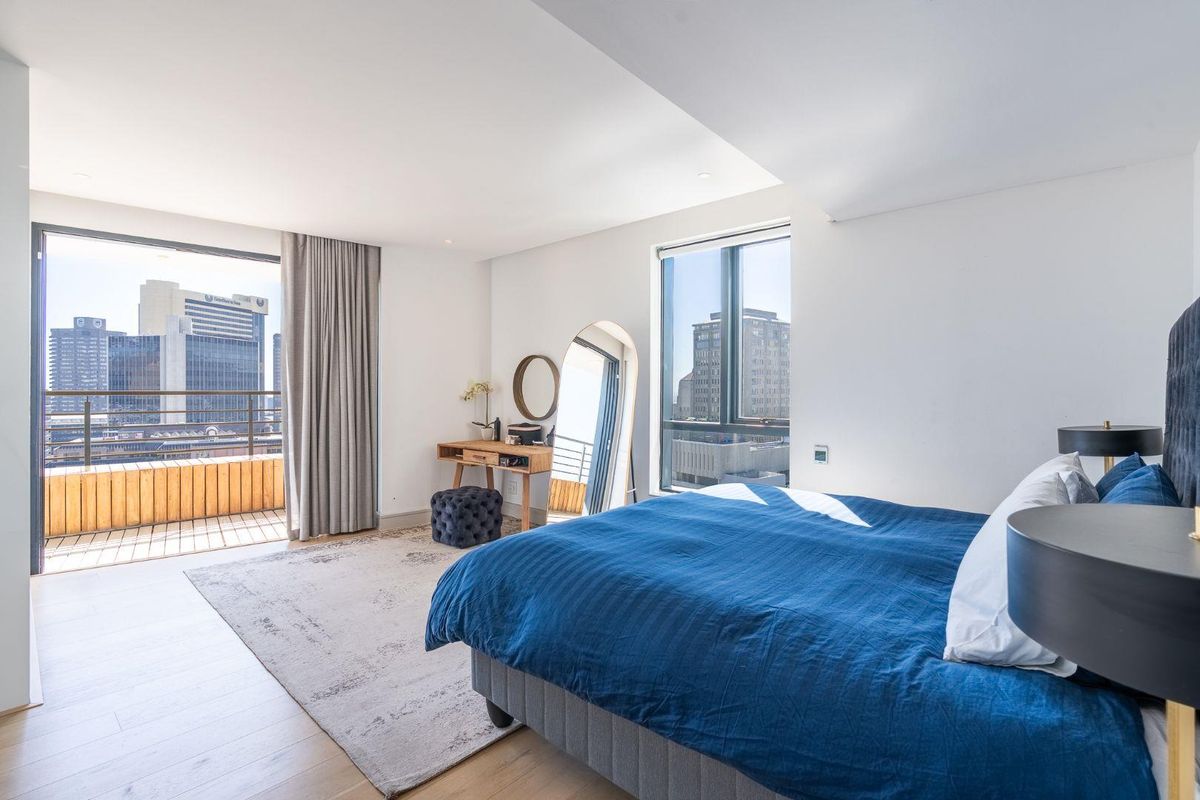 Spacious modern bedroom featuring floor-to-ceiling windows, light timber flooring, and direct access to a private balcony with city views.