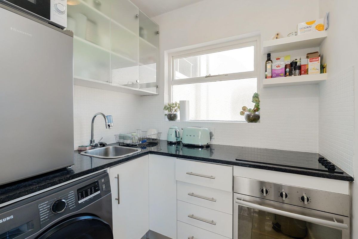 Compact modern kitchen featuring white cabinetry, black granite countertops, integrated oven, ceramic hob, and a tiled backsplash with floating shelving.