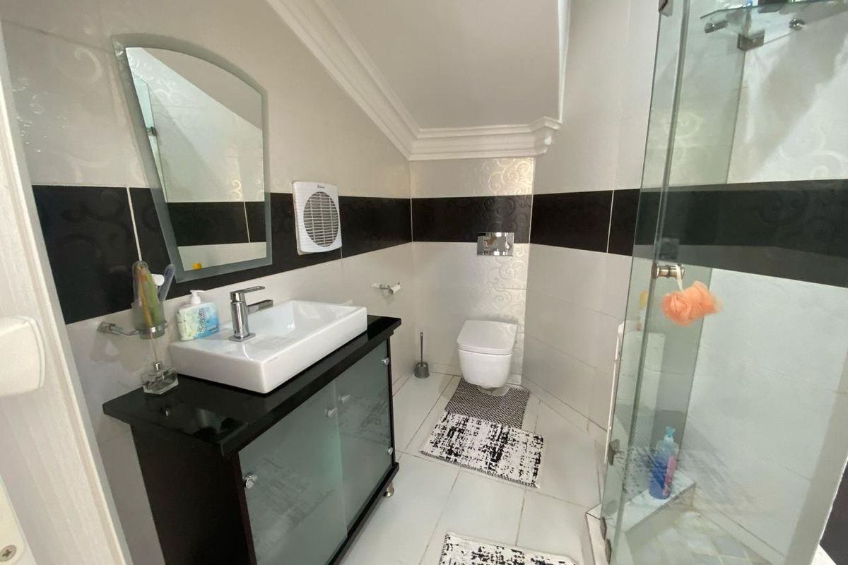 A compact modern bathroom featuring a wall-mounted toilet, a glass-enclosed shower, and a vanity unit with a vessel sink.