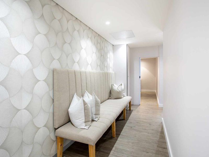 A well-lit, modern hallway featuring patterned wallpaper, recessed ceiling lighting, and wood-look flooring, leading to an adjacent interior space.