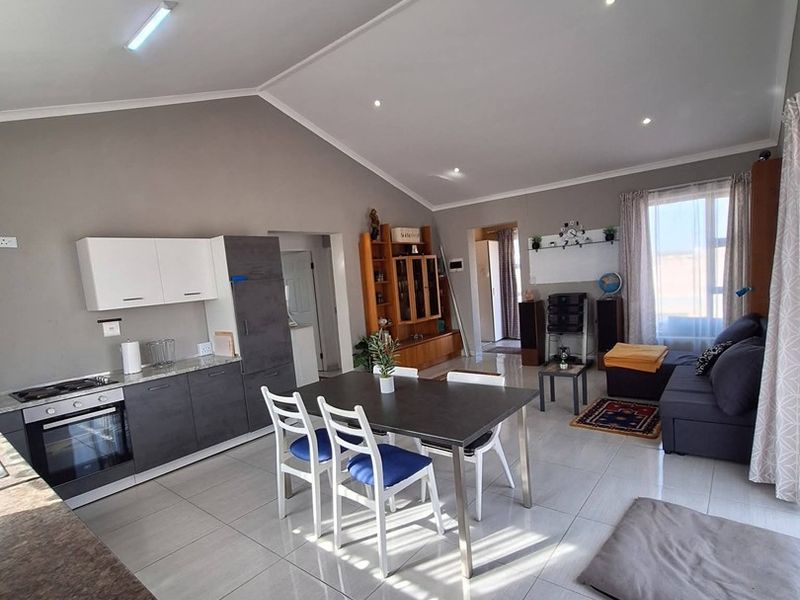 An open-plan living and kitchen area featuring modern cabinetry, integrated appliances, tiled flooring, and a spacious vaulted ceiling design.