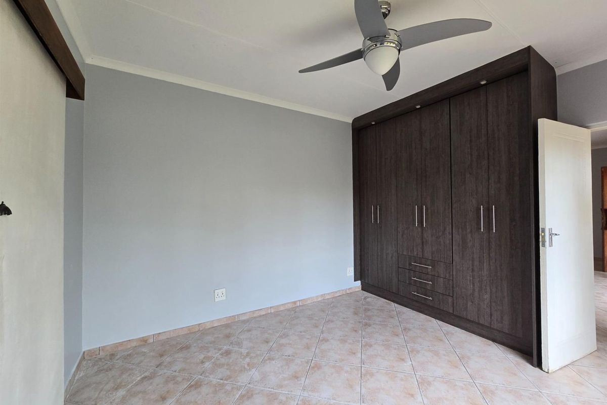 A clean, empty bedroom featuring dark wood built-in cupboards, a modern ceiling fan, and neutral tiled flooring.