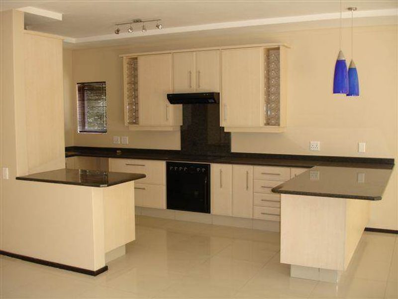 A clean, modern kitchen featuring light wood cabinetry, dark granite countertops, integrated oven, and a functional breakfast nook layout.