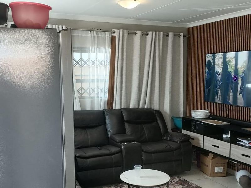 A living room featuring decorative slatted timber wall paneling, tiled flooring, and a window fitted with a security gate.