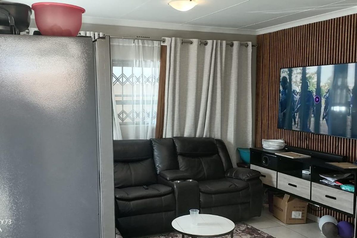 A living room featuring decorative slatted timber wall paneling, tiled flooring, and a window fitted with a security gate.
