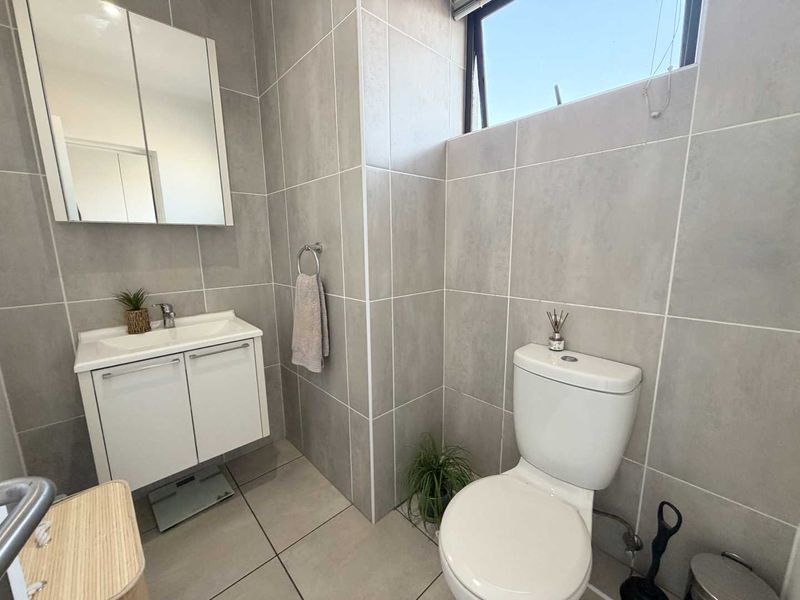 Modern bathroom featuring neutral grey wall and floor tiles, a white vanity cabinet with basin, and a wall-mounted mirror cabinet.