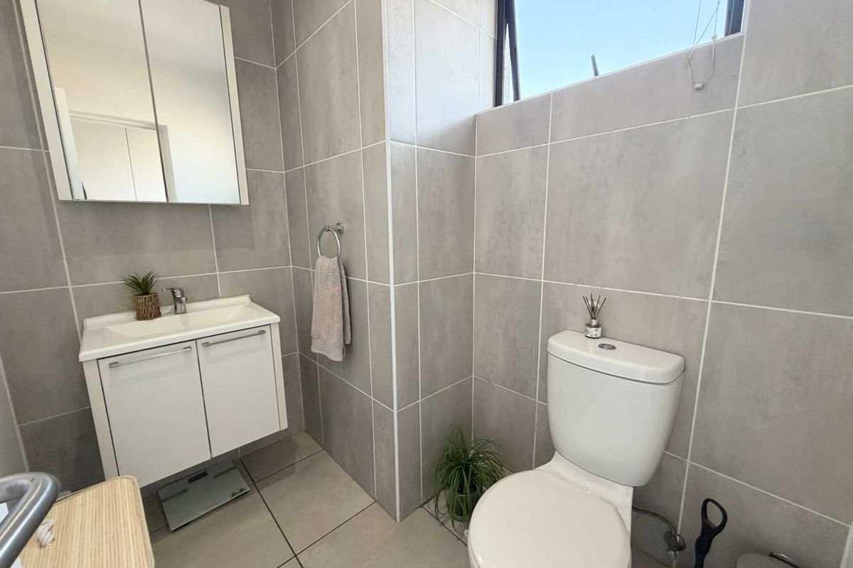 Modern bathroom featuring neutral grey wall and floor tiles, a white vanity cabinet with basin, and a wall-mounted mirror cabinet.