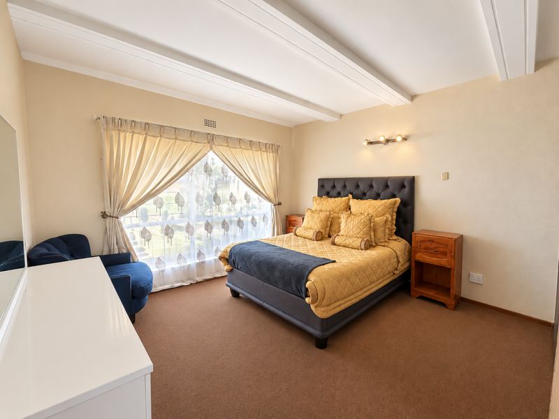 A well-maintained bedroom featuring carpeted flooring, decorative ceiling beams, and a wall-mounted light fixture, offering a comfortable and functional living space.