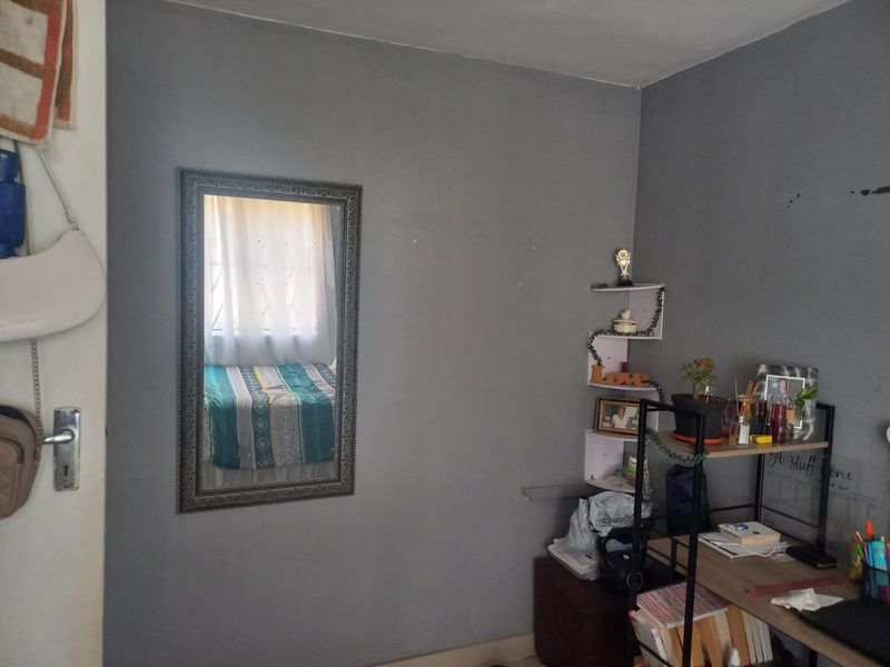 A bedroom featuring grey painted walls, a window with curtains, and a door, providing a functional space for rest.