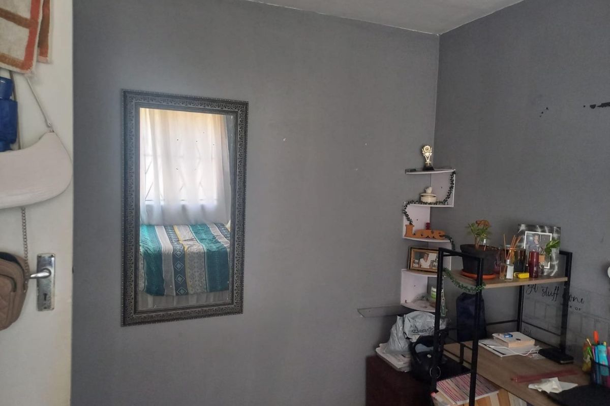 A bedroom featuring grey painted walls, a window with curtains, and a door, providing a functional space for rest.
