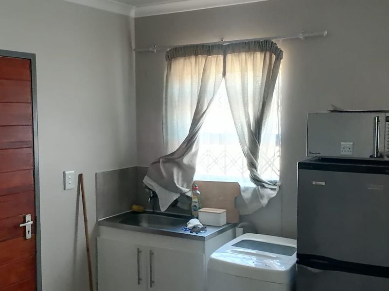 A functional scullery or utility area featuring a stainless steel sink, base cabinetry, and tiled splashback, providing practical space for laundry or food preparation.