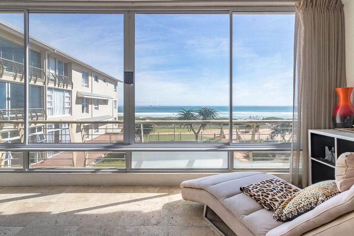 A bright living space featuring expansive floor-to-ceiling windows that offer a clear, direct view of the ocean and coastline.