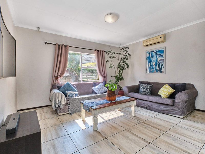 A comfortable living room featuring tiled flooring, a wall-mounted air conditioning unit, and natural light through a window with curtain fittings.