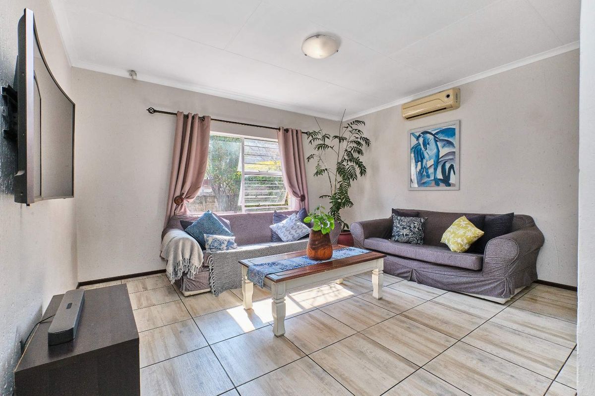 A comfortable living room featuring tiled flooring, a wall-mounted air conditioning unit, and natural light through a window with curtain fittings.