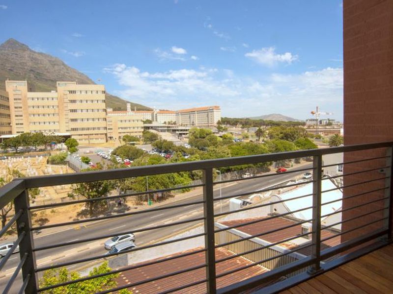 A balcony featuring timber decking and a modern metal railing, offering an elevated urban view towards the mountain.