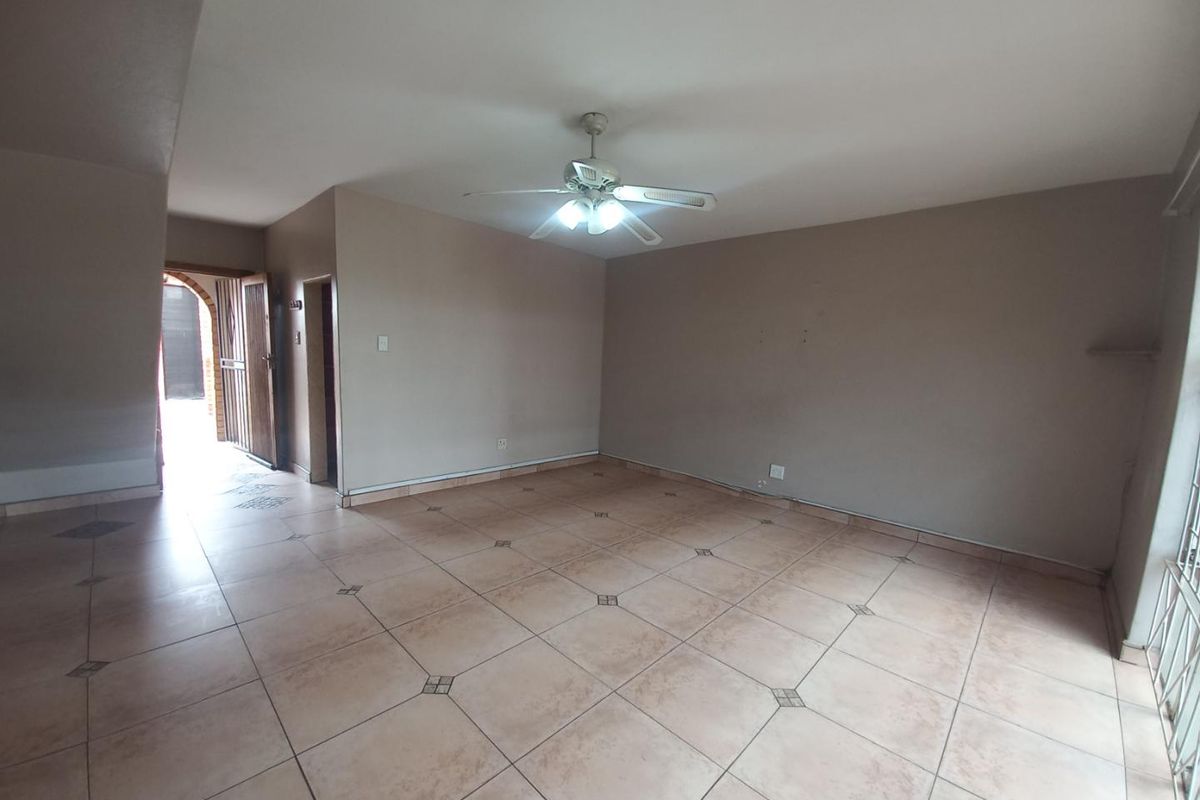 A spacious, empty living area featuring neutral tiled flooring, a ceiling fan, and direct access to an exterior entrance.