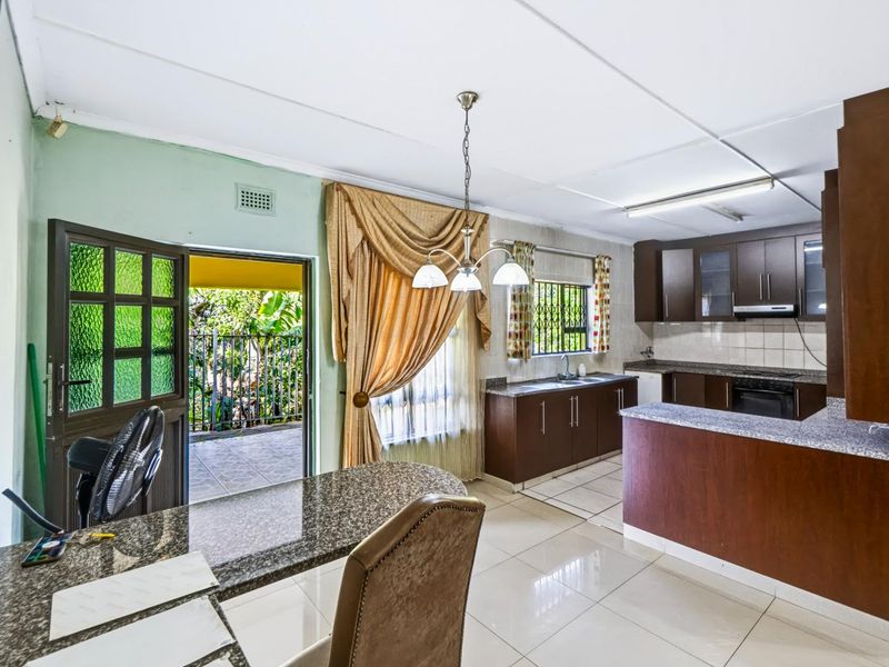 Open plan kitchen and dining area featuring granite countertops, dark wood cabinetry, tiled flooring, and direct access to an outdoor patio area.