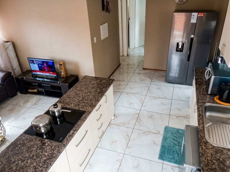 An open-plan kitchen and living area featuring modern tiled flooring, built-in cabinetry with laminate countertops, and a built-in electric hob.