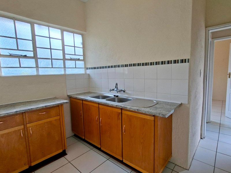 A functional kitchen area featuring timber cabinetry, laminate countertops, a double bowl sink, and tiled splashbacks with ceramic floor tiles.