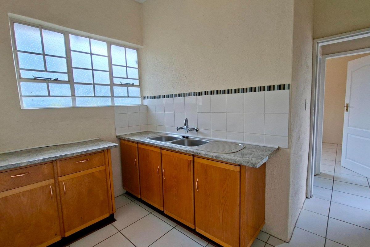 A functional kitchen area featuring timber cabinetry, laminate countertops, a double bowl sink, and tiled splashbacks with ceramic floor tiles.