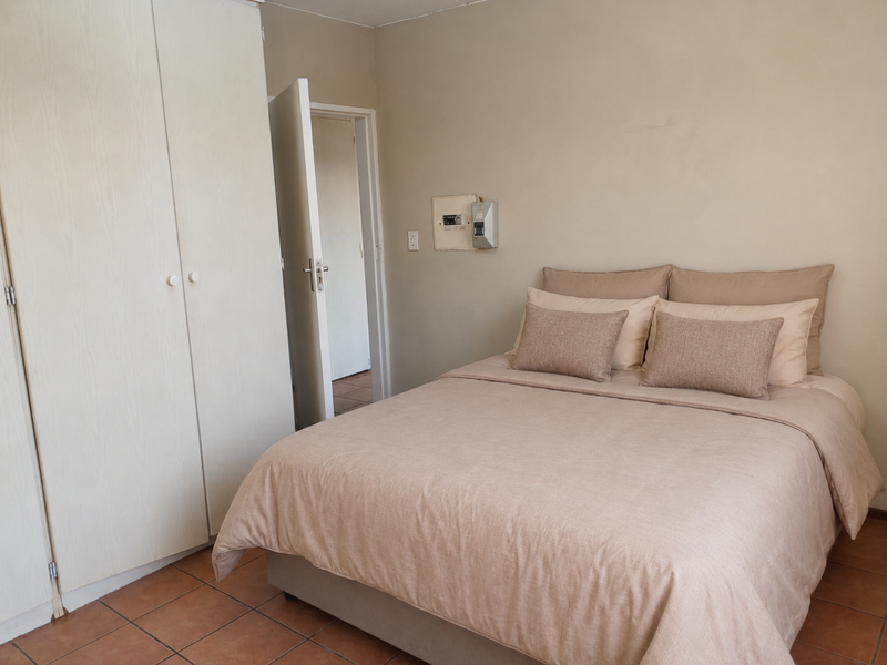 A bedroom featuring built-in wardrobes, tiled flooring, and an exposed electrical distribution board on the wall.