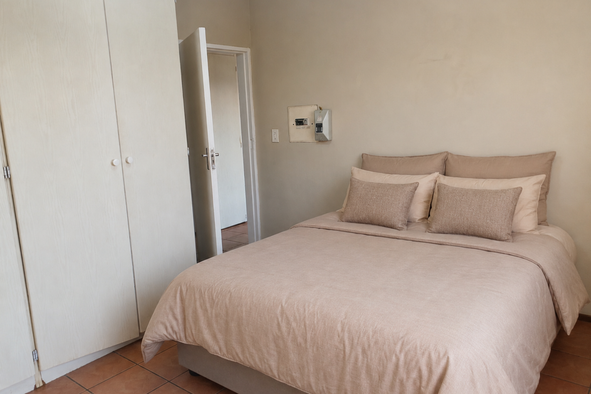 A bedroom featuring built-in wardrobes, tiled flooring, and an exposed electrical distribution board on the wall.