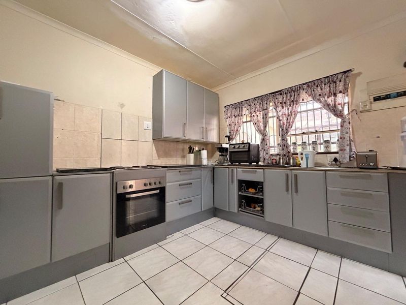 A functional kitchen featuring grey built-in cabinetry, an integrated electric oven and hob, tiled flooring, and a tiled backsplash.