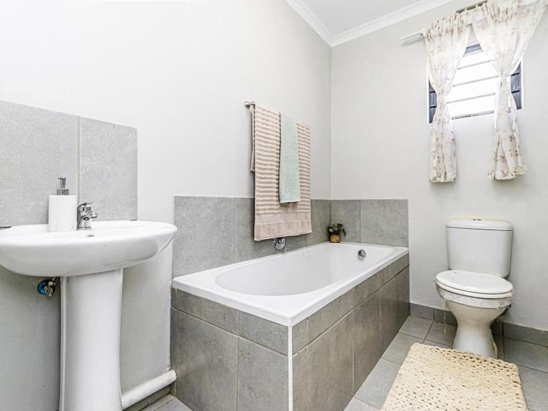 A functional bathroom featuring a pedestal washbasin, a built-in bathtub with tiled surround, and a standard toilet with neutral wall and floor finishes.