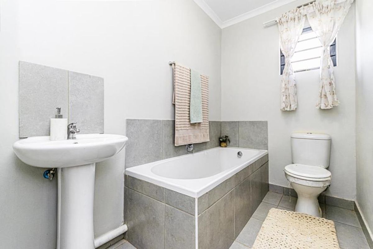 A functional bathroom featuring a pedestal washbasin, a built-in bathtub with tiled surround, and a standard toilet with neutral wall and floor finishes.