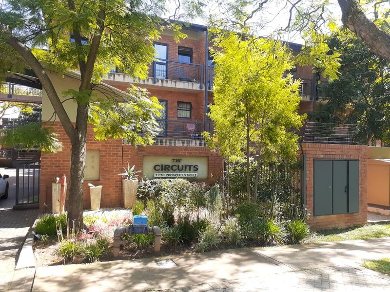 Front elevation of The Circuits apartment complex, featuring a brick facade, balconies, and established garden landscaping.