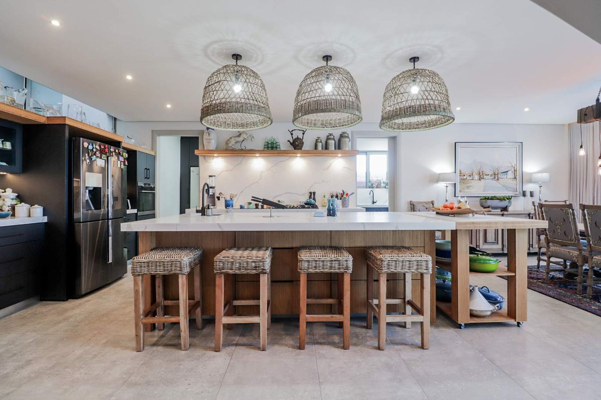 Modern kitchen featuring a large central island with stone countertops, custom cabinetry, floating shelving, and elegant pendant lighting in an open-plan layout.