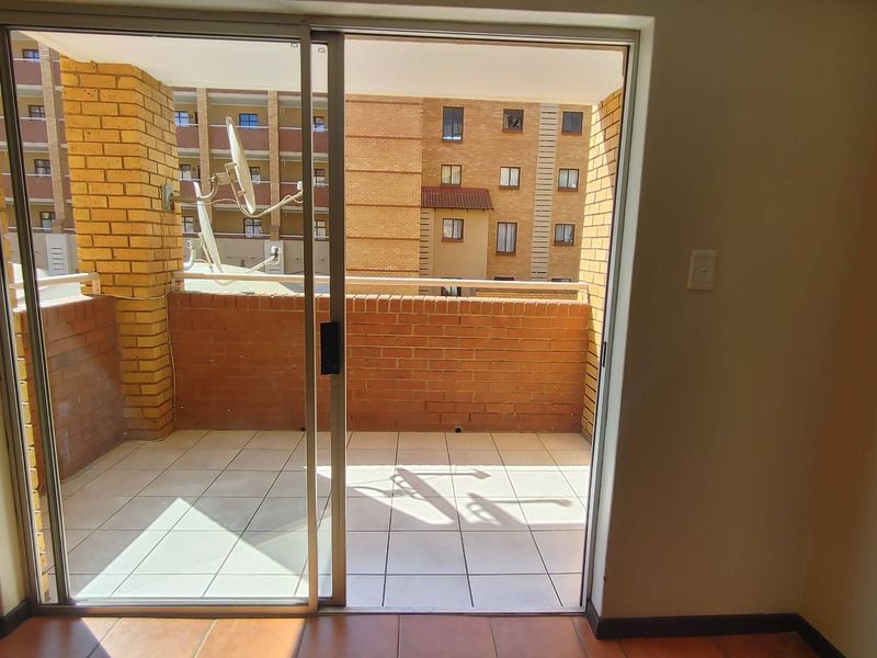 A private balcony featuring tiled flooring and a brick balustrade, accessible through a sliding glass door from the interior living space.