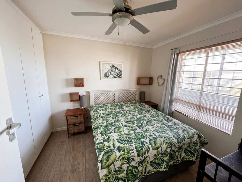 A well-maintained bedroom featuring built-in cupboards, a ceiling fan, and laminate flooring, complemented by natural light through venetian blinds.