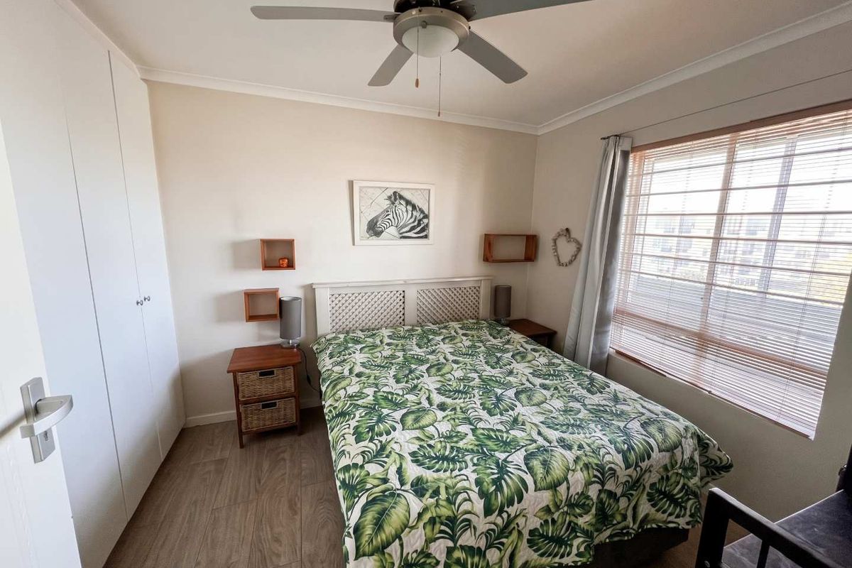 A well-maintained bedroom featuring built-in cupboards, a ceiling fan, and laminate flooring, complemented by natural light through venetian blinds.
